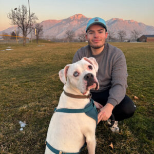 Daniel and his dog looking at the camera while standing in a field with mountains in the background.